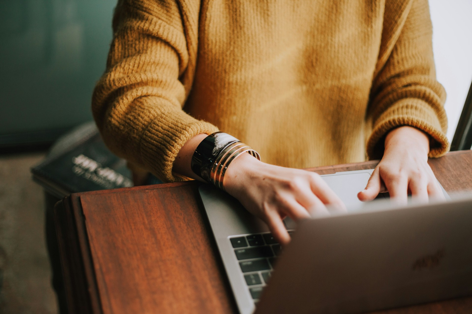 Close up of a woman wearing a yellow jumper typing on a laptop